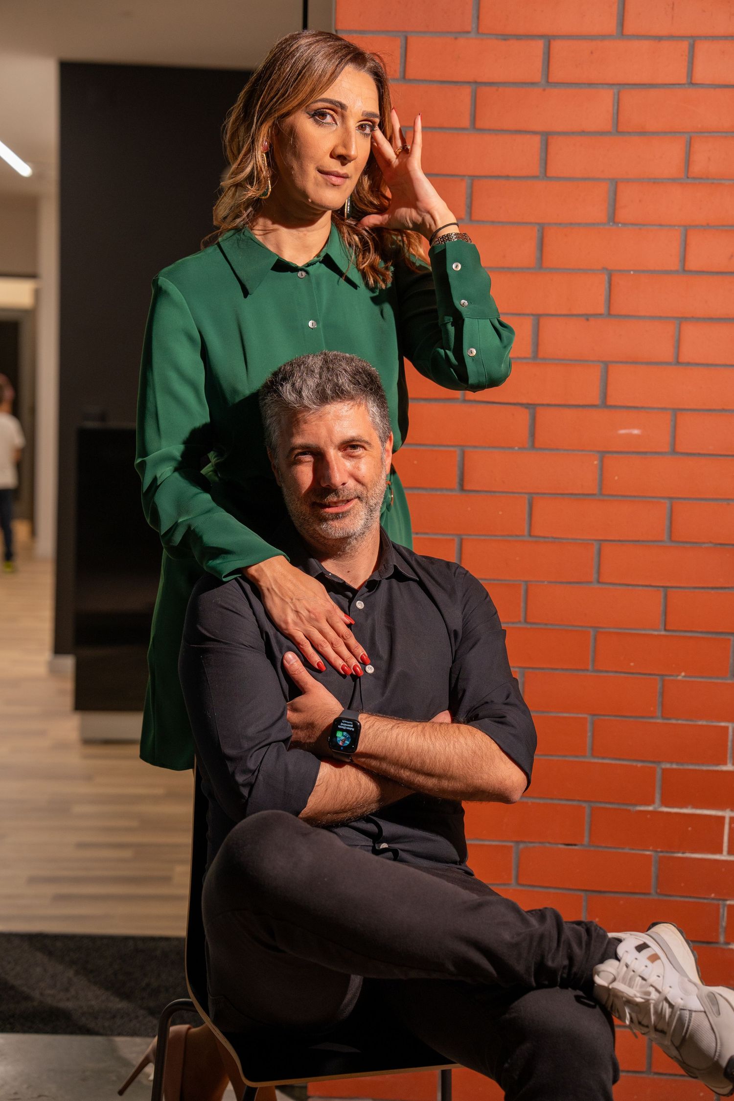 A couple in green and navy outfits pose against a brick wall in a romantic photoshoot.