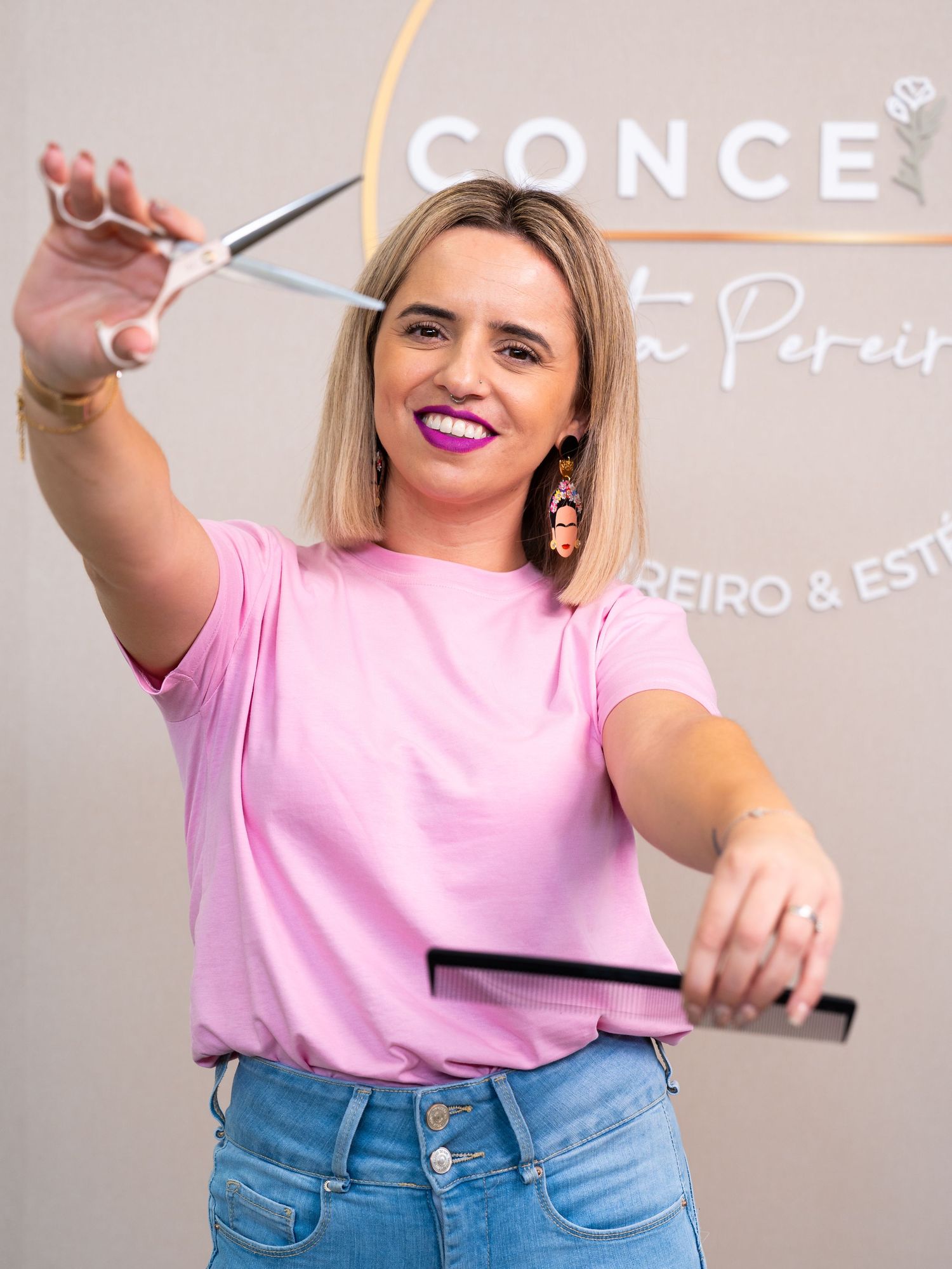 A stylist in pink shirt and jeans demonstrates hair care techniques in a salon.