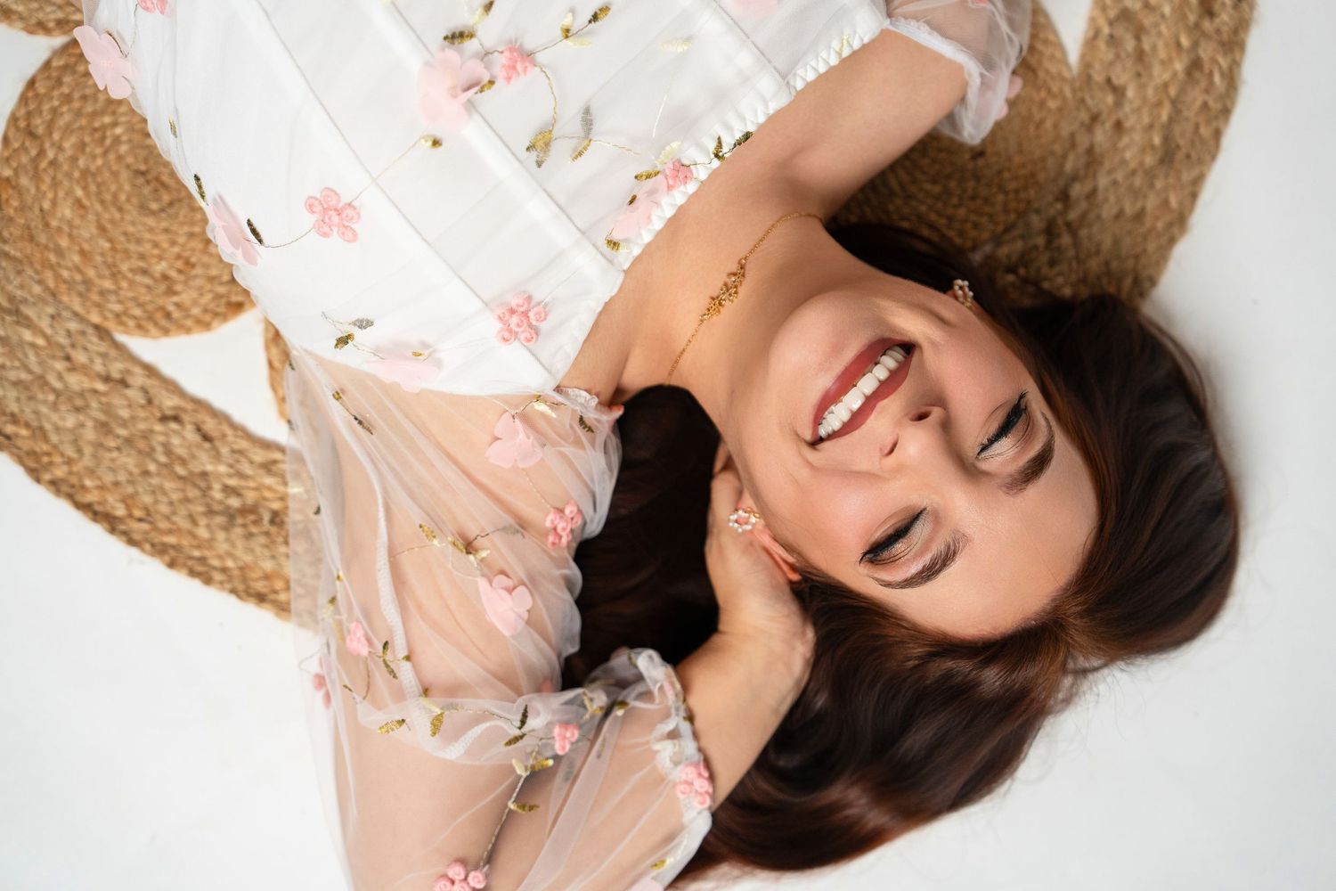 A lifestyle portrait with a straw hat and delicate floral top against white background.