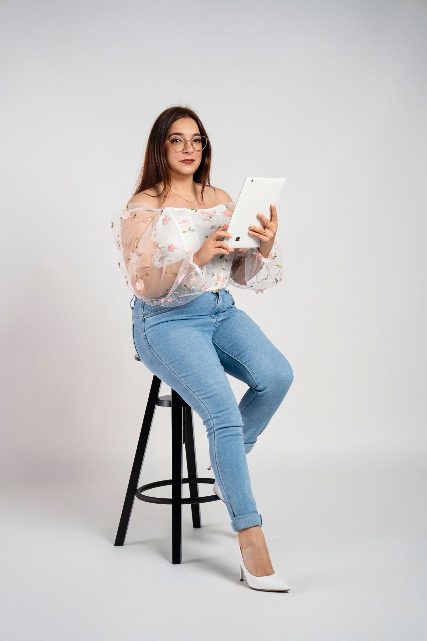 A casual portrait session featuring denim jeans and a sheer floral top on a white backdrop.