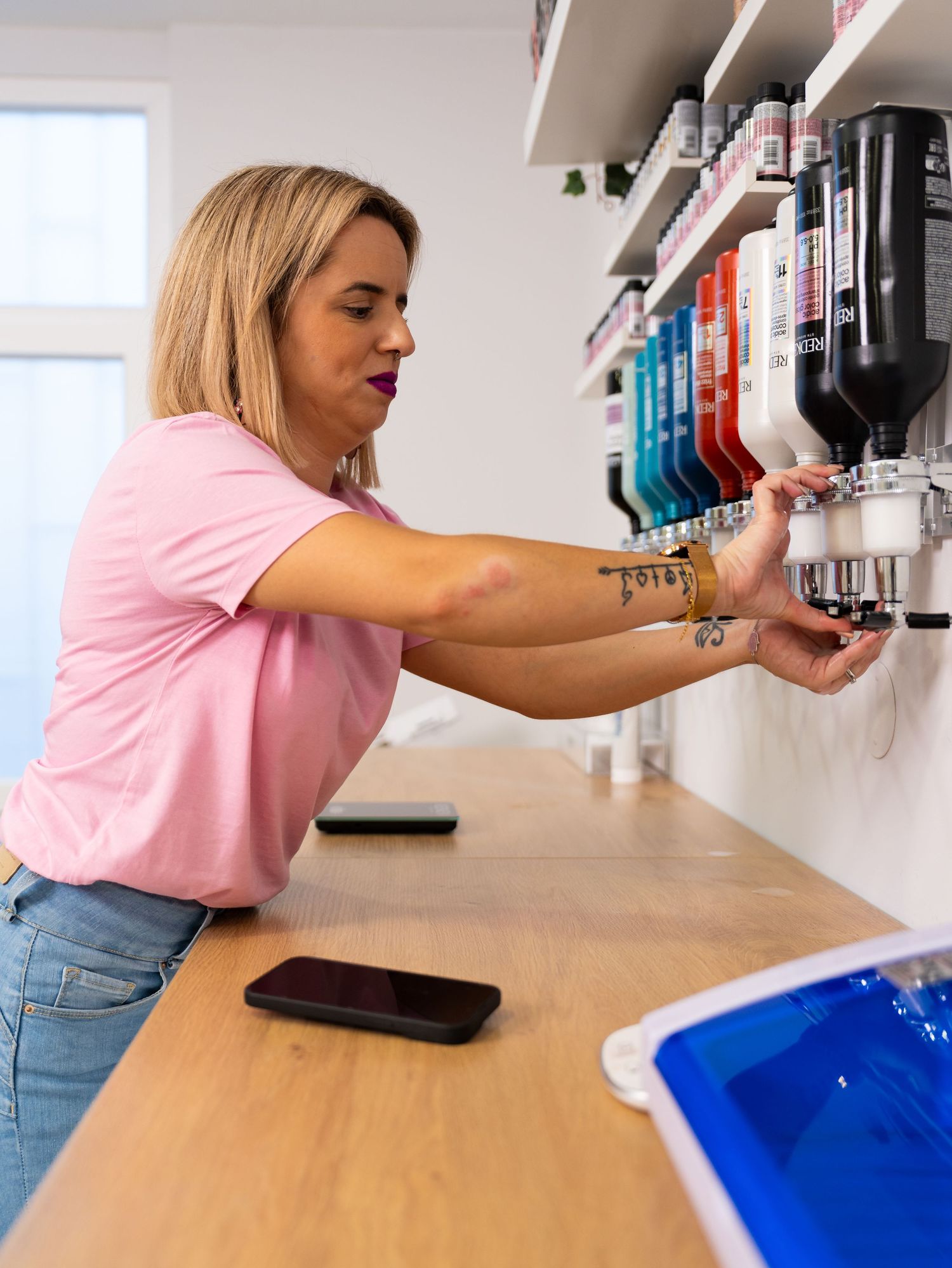 A person in pink shirt dispenses product from wall-mounted containers.