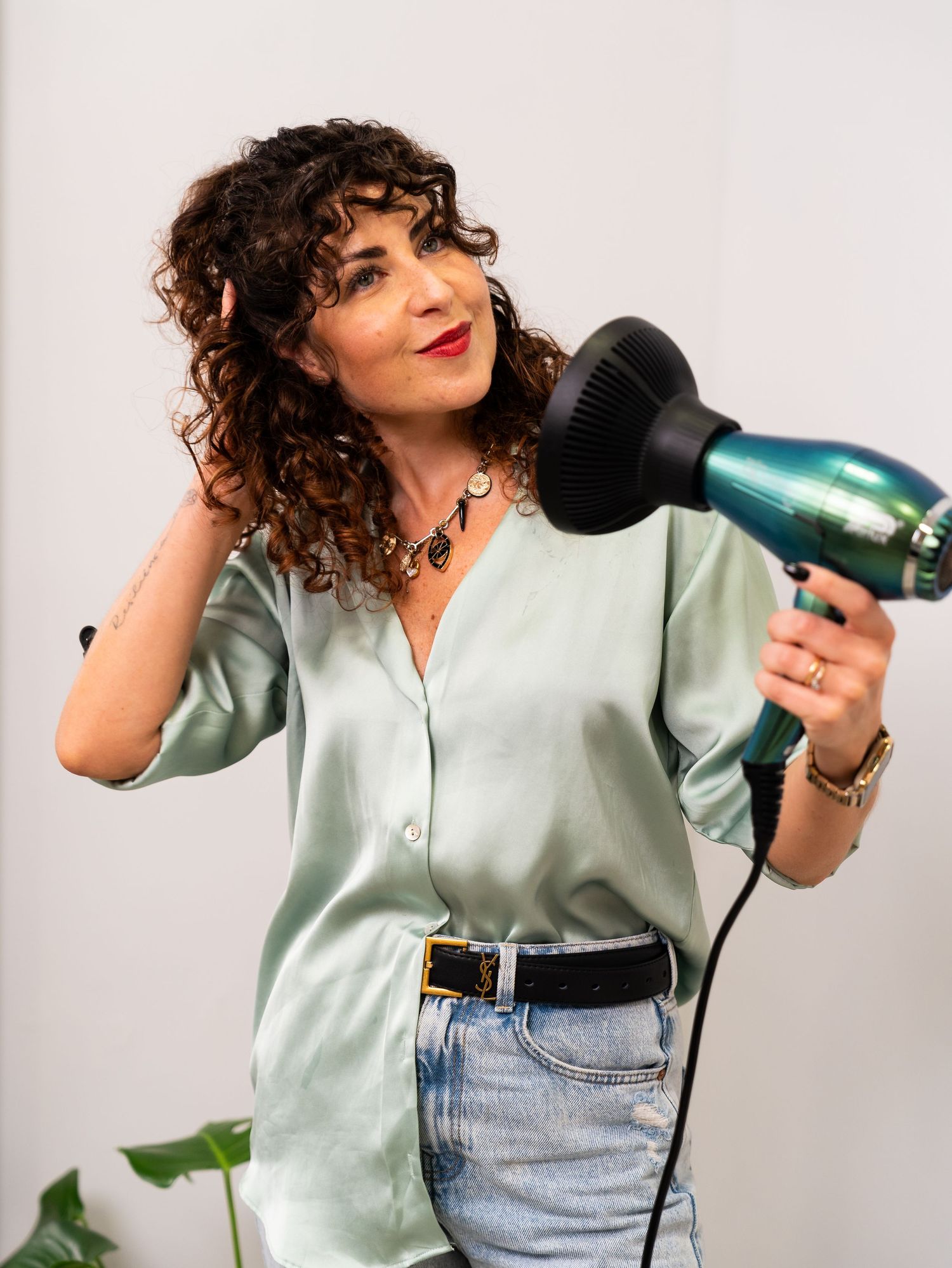 A stylist in mint green shirt uses a turquoise hair dryer while styling.