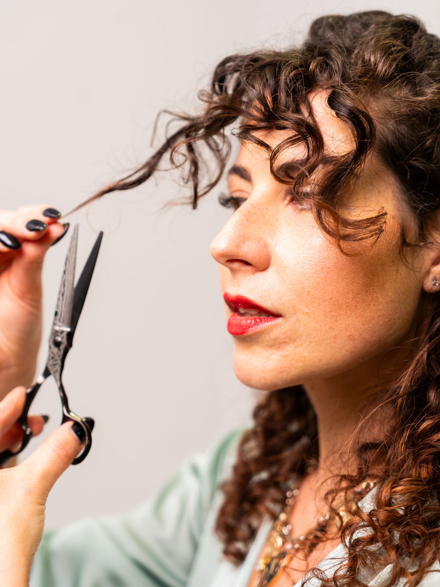 Close-up of styling scissors being used on curly hair against white background.