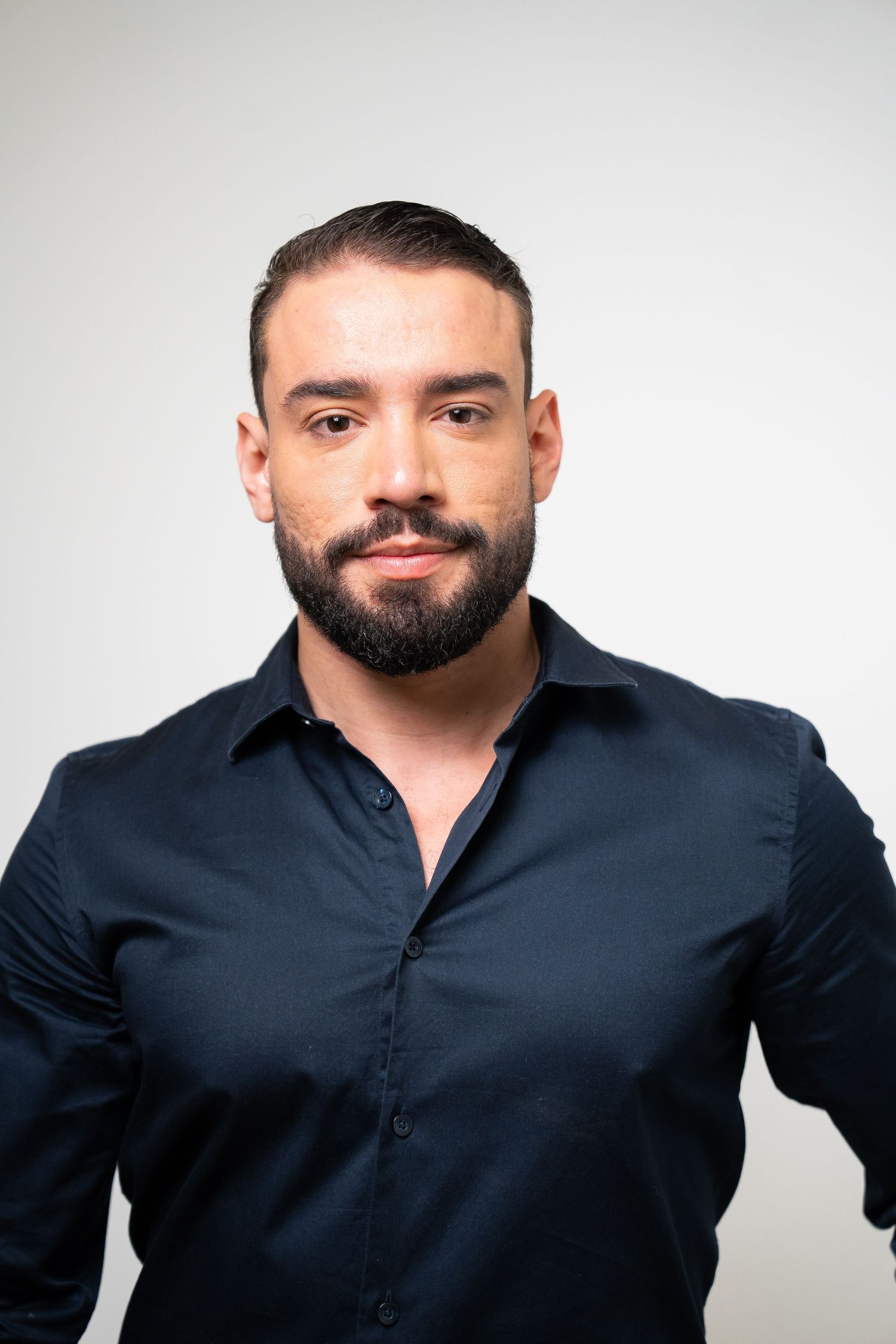 Business casual portraits of someone in dark shirt posing confidently against white backdrop.