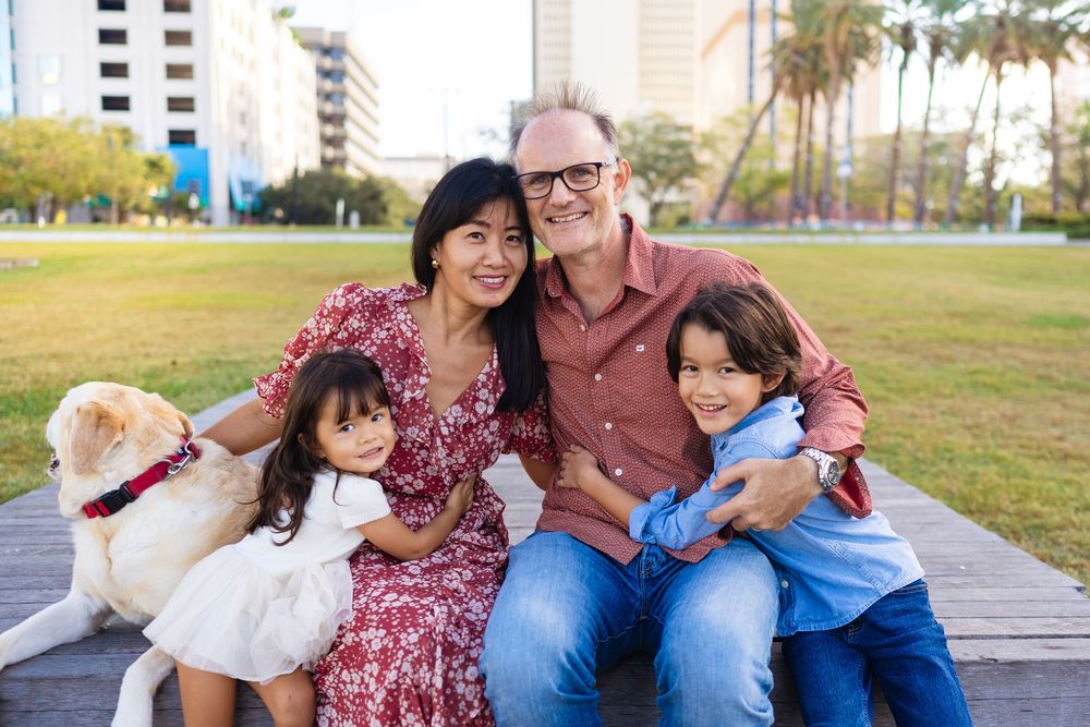 Family sitting together on a park bench during golden hour at a grassy outdoor area.