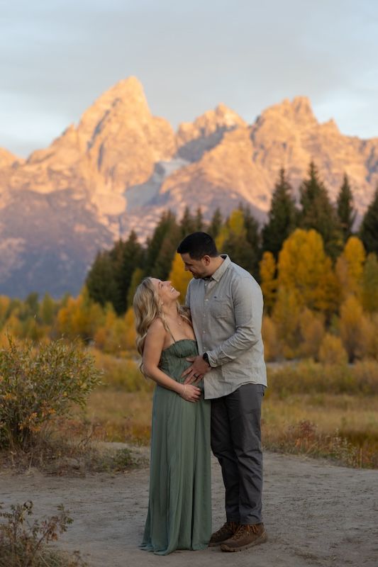 A couple shares an intimate moment at sunset in front of the majestic Grand Teton mountains with fall foliage.