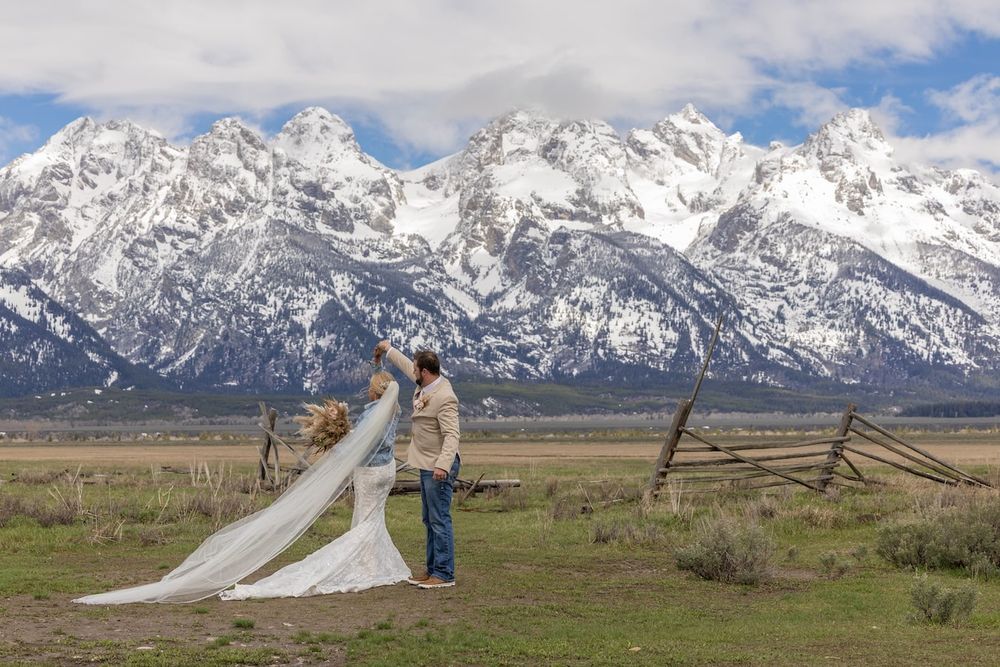 A bride and groom pose for wedding photos against the majestic snow-capped Grand Teton mountains on a clear spring day.