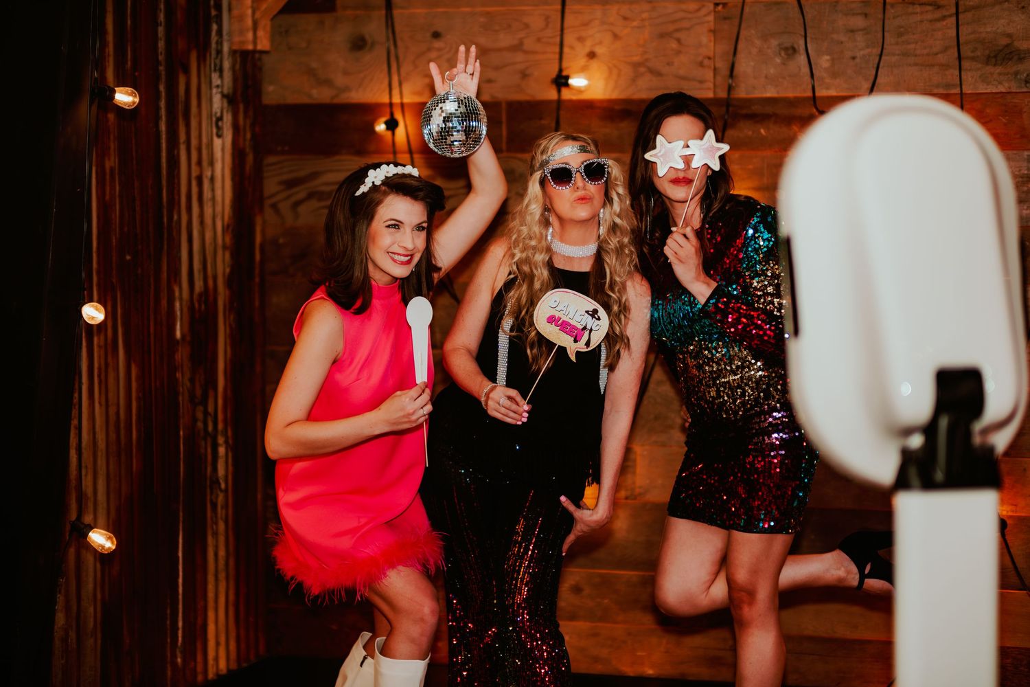 Three friends dancing together at a party wearing sparkly party dresses and festive accessories.