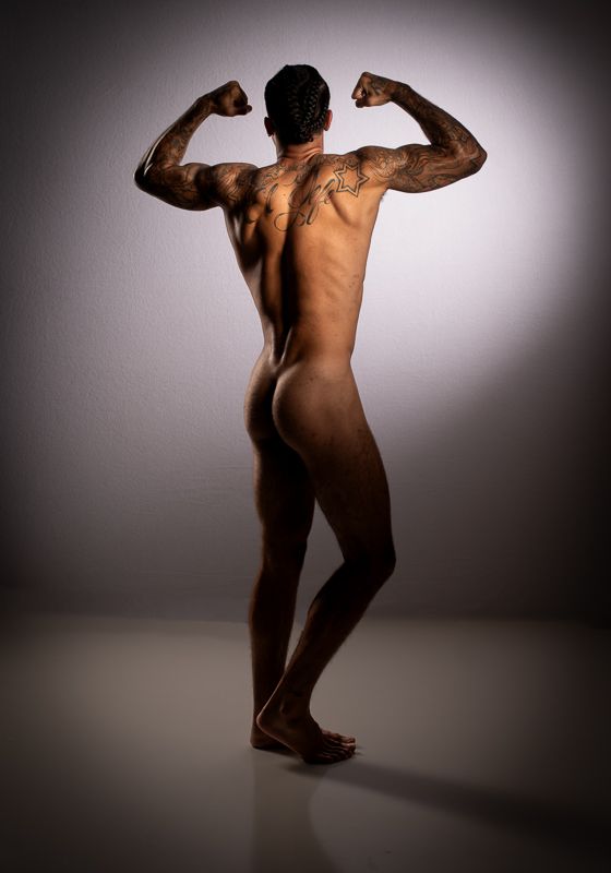 Artistic nude figure in dramatic lighting performs dynamic dance movements against dark studio backdrop.