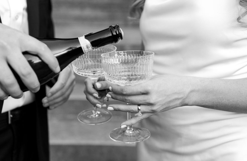 A person pours champagne into vintage coupe glasses in an elegant black and white photograph.