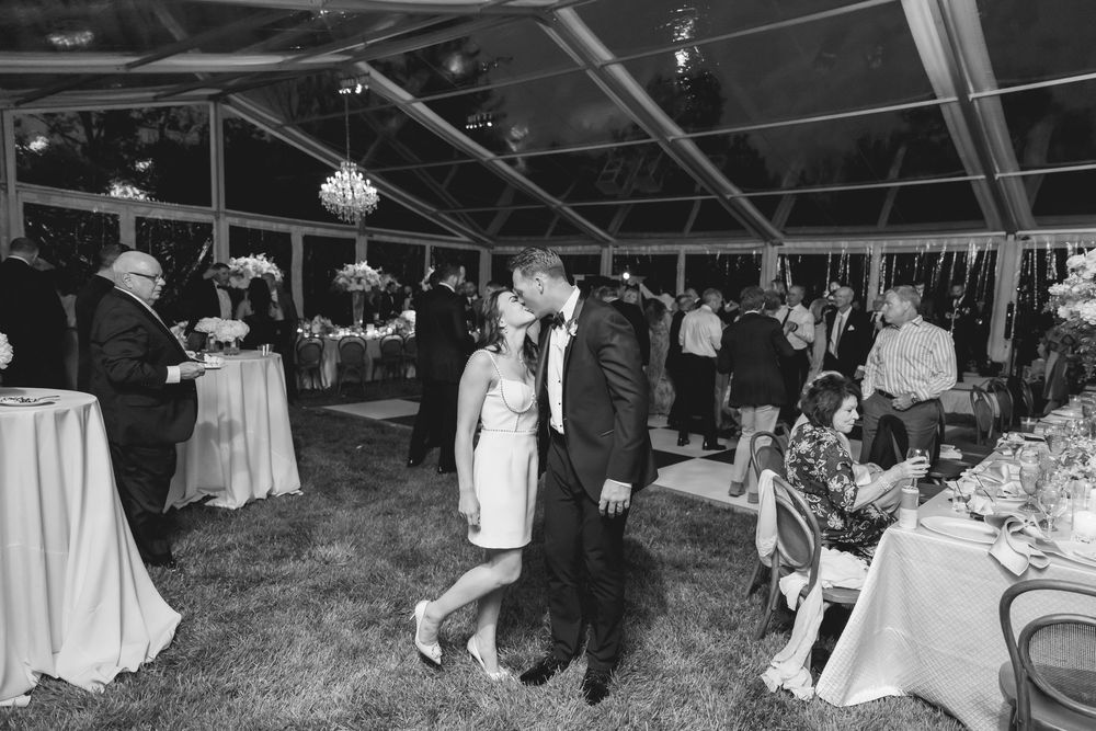 Black and white panoramic photo of an elegant wedding reception under a tent with tables, decor and guests mingling.