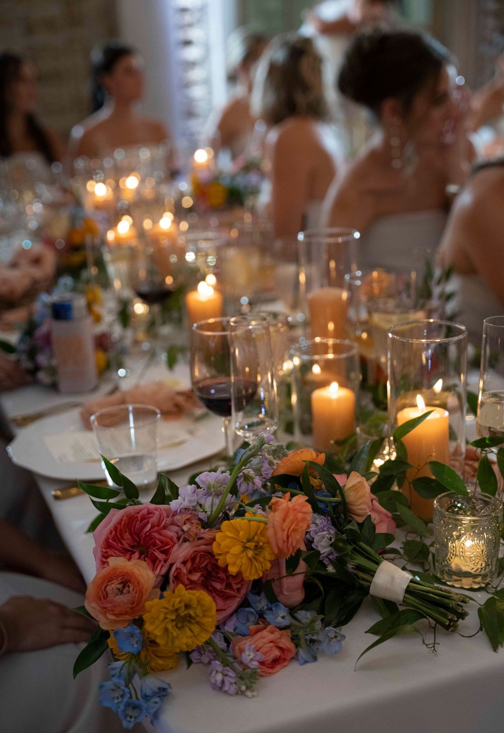 Elegant wedding reception table decorated with candlelight, colorful floral arrangements and place settings.