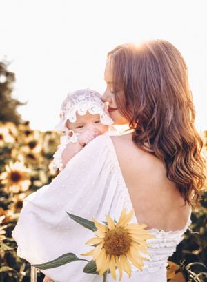 newborn baby, little girl with bonnet, looking over mom's shoulder, sunflowers, mom kissing baby's cheek, family photographer, Moncton.