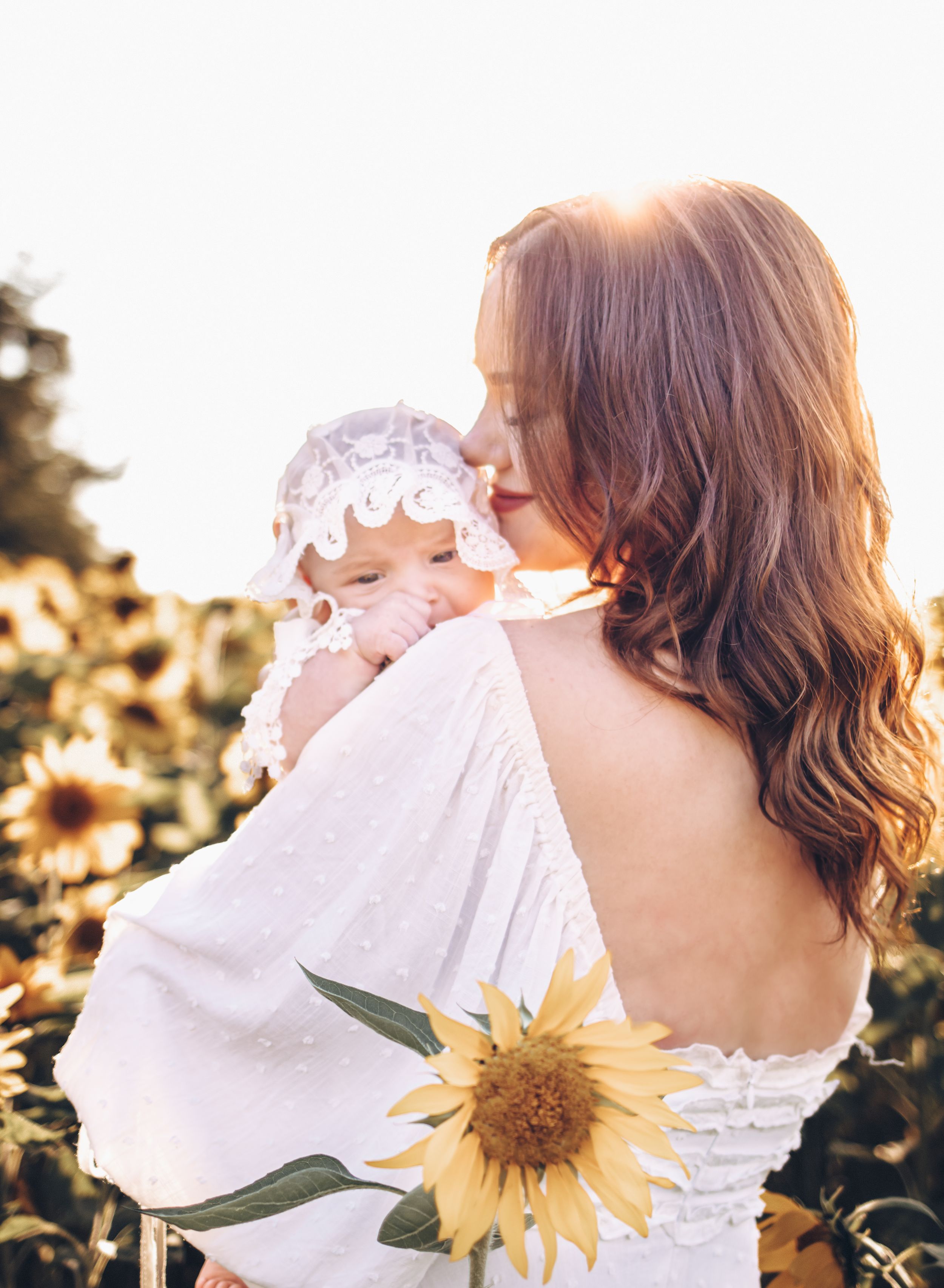 newborn baby, little girl with bonnet, looking over mom's shoulder, sunflowers, mom kissing baby's cheek, family photographer, Moncton.