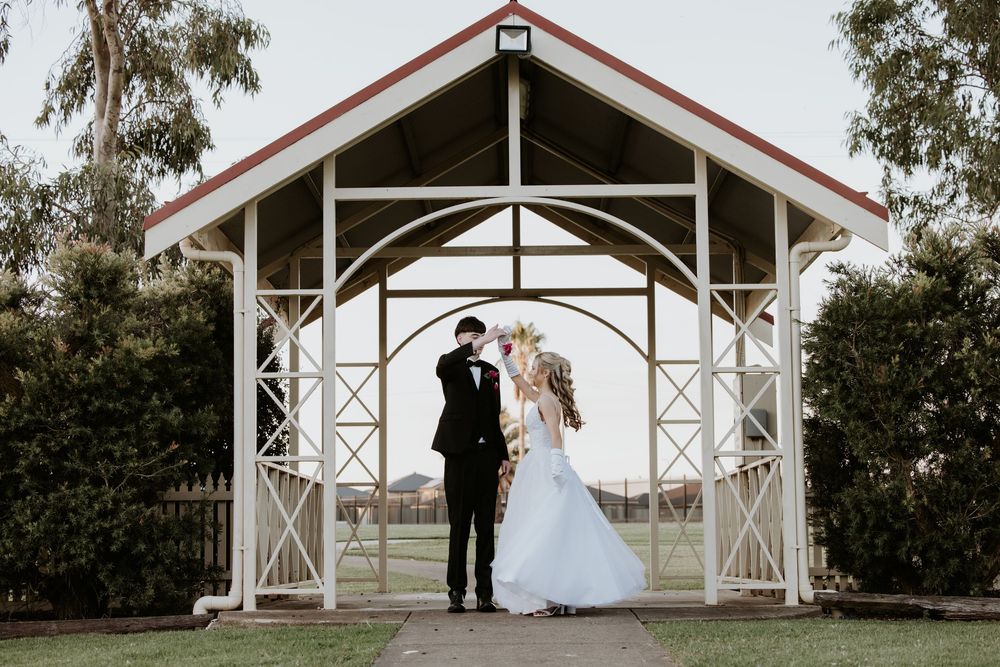 A white wedding chapel with wooden beams and cross details stands nestled among trees on a sunny day.