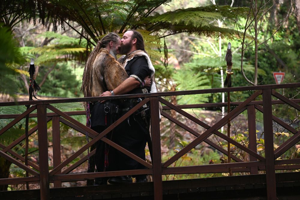 Romantic couple embraces on a wooden bridge surrounded by lush forest scenery.