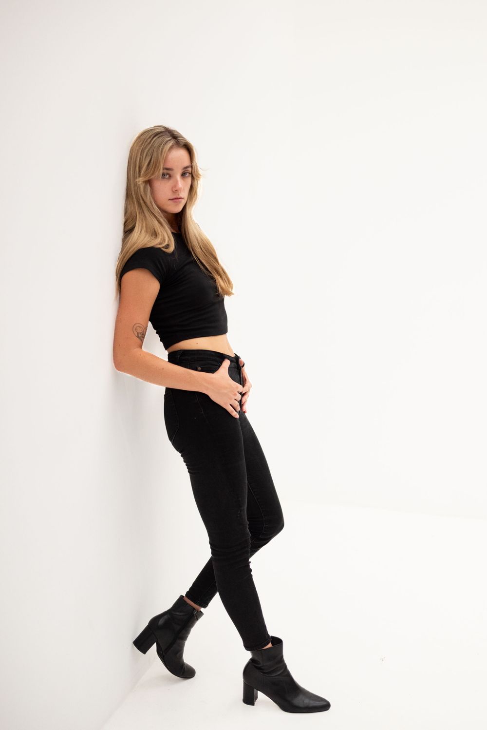 Fashion model in all black outfit poses against white background.