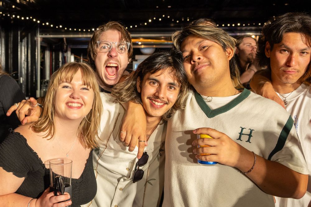 Group of friends laughing and celebrating together under string lights at night.
