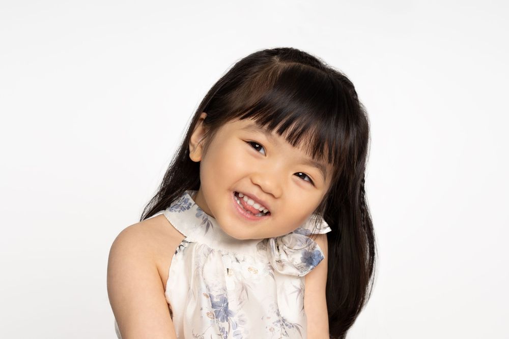 Child in white floral dress smiling at camera.