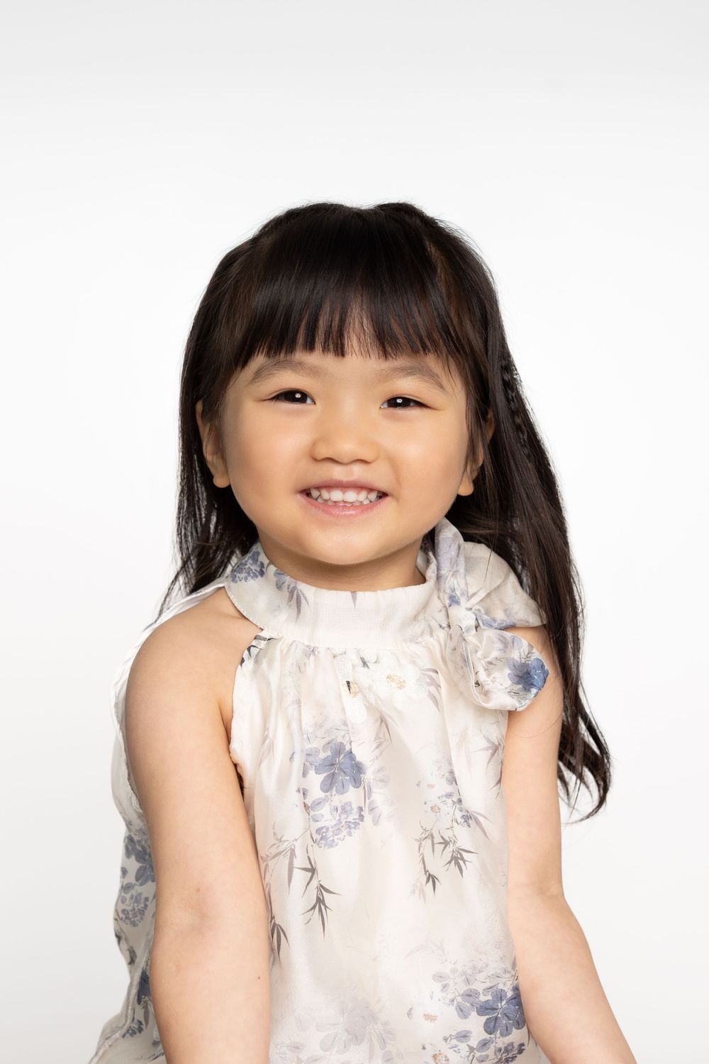 Child wearing floral print dress poses against white background.