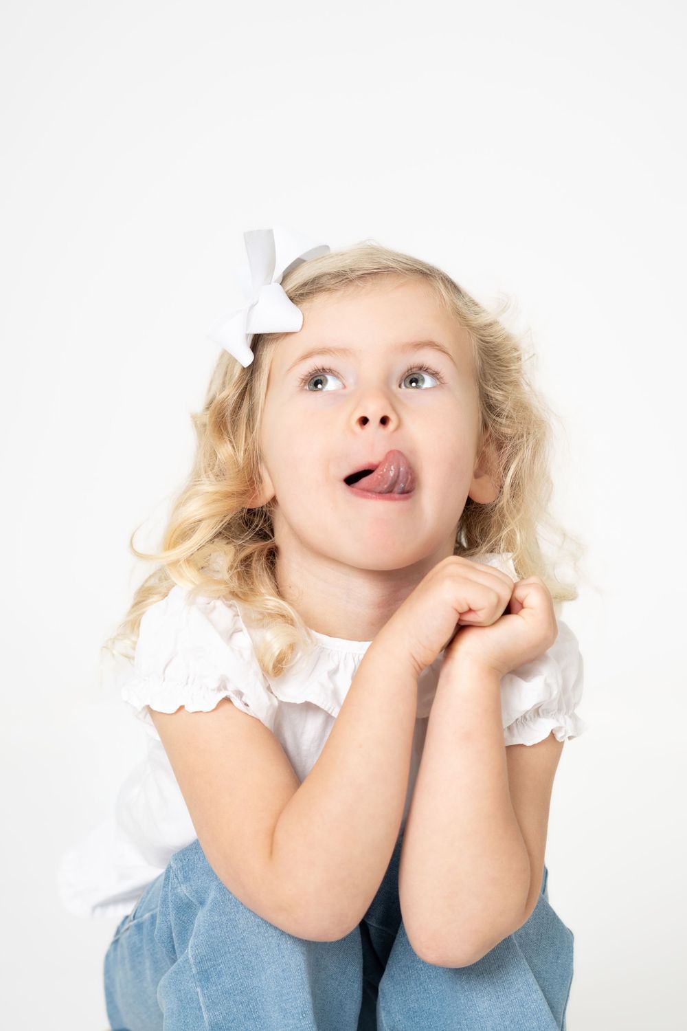 A series of playful expressions showing a young child in a white top and blue outfit making silly faces against white background.