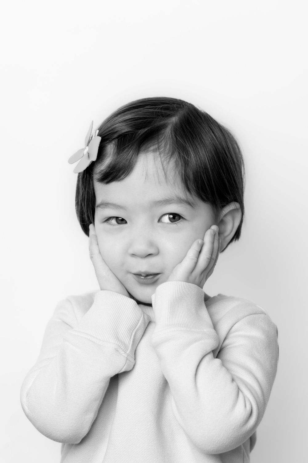 Three black and white photos show a child in a white sweater making playful expressions against a light background.