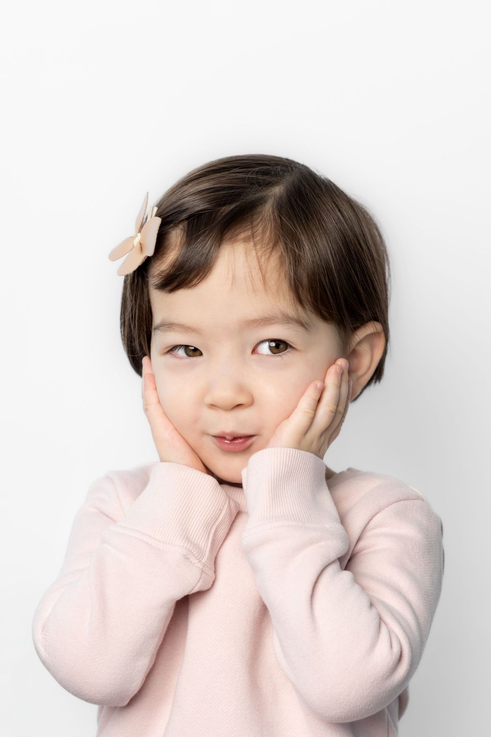 Three photos show a child in a pink sweater making playful expressions against a white background.