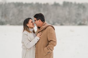 Romantic winter engagement photo session showing couple in warm coats embracing in snowy landscape.
