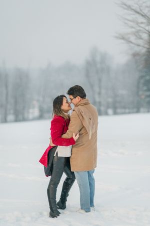 A couple embraces lovingly in a snowy winter landscape during a romantic photoshoot.