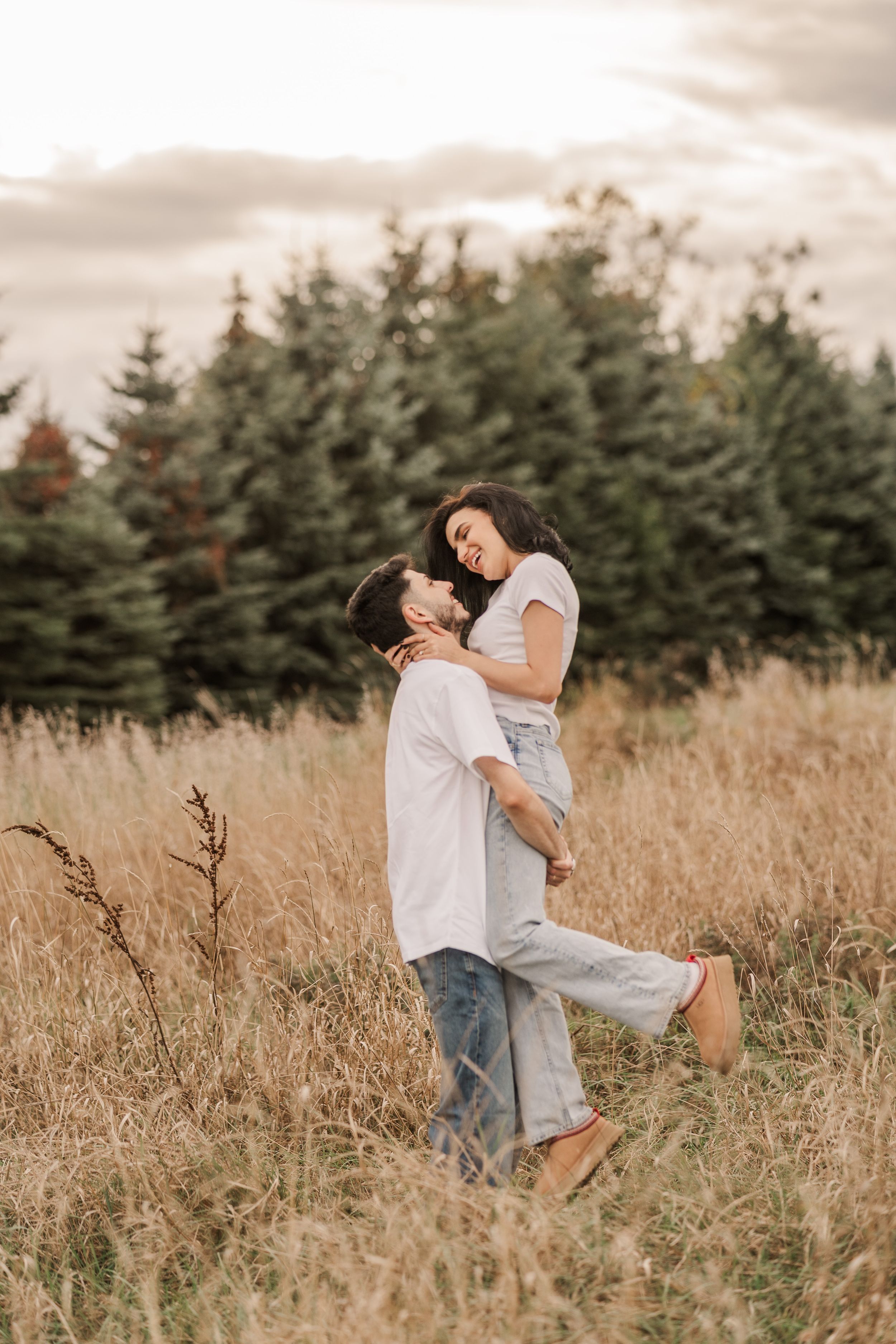Playful couple dancing and twirling in a golden wheat field at sunset.