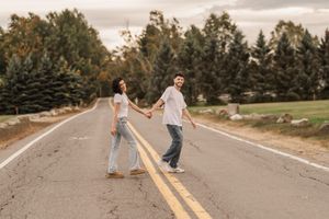 Couple walking and playing on a rural road surrounded by autumn trees and fields.