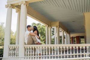 A couple sits intimately together on a white columned porch with ornate balustrades and a blue ceiling.