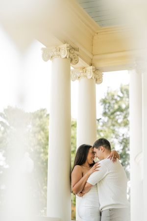 A romantic couple shares a tender moment while dancing together on an elegant white columned porch.