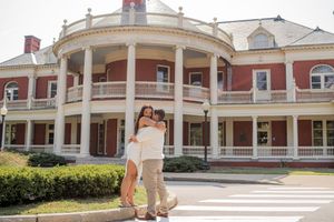 Panoramic view of a grand colonial-style building with white columns and red brick exterior spanning multiple connected sections.