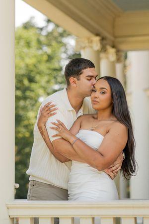 A romantic couple embraces on a white columned porch during a photo session.