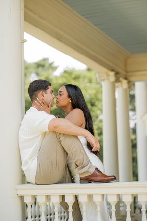 A couple shares an intimate moment while sitting on a railing of a classical columned porch.