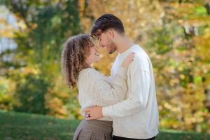 Romantic autumn couple embracing in park with fall foliage backdrop.