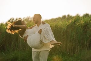A romantic couple embraces in a golden sunset field, with tall grass swaying in the background.