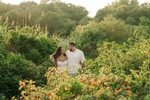 A romantic sunset engagement photo session in a wildflower field with golden light filtering through the foliage.