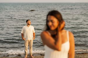 A couple shares an intimate moment on a beach at sunset with waves crashing in the background.