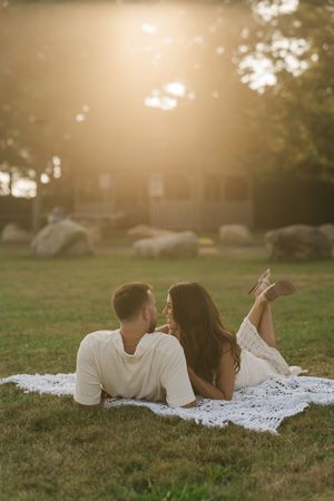 Couple relaxing together on a white blanket in a grassy field during golden hour sunset.
