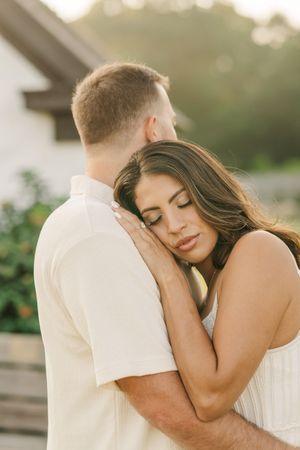 A romantic couple embraces tenderly in soft natural lighting during an outdoor photoshoot.