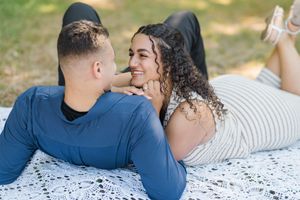A couple lying on a white blanket outdoors sharing an intimate moment while enjoying a sunny day.