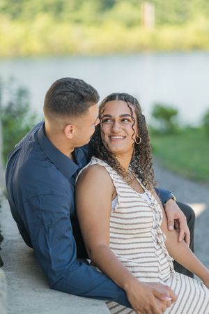 A couple shares an intimate moment while sitting together outdoors near a waterfront.