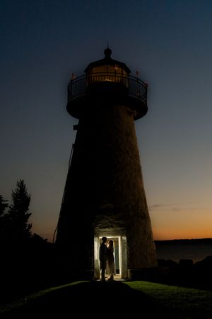 A silhouetted lighthouse tower photographed at dusk with a warm orange sunset glow in the background.
