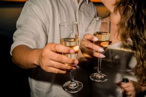Close-up shot of hands toasting with wine glasses at a social gathering.