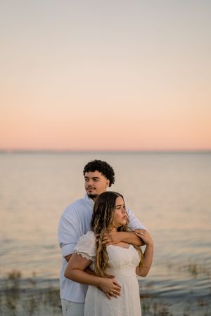 A couple shares an intimate moment at the beach during golden hour with the ocean behind them.
