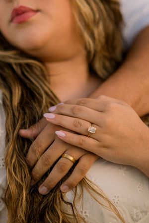 Close-up view of hands wearing engagement ring and wedding band against white lace fabric background.