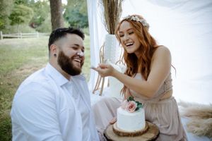 A couple sharing a joyful moment while cutting cake at an outdoor celebration.