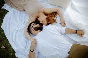 A couple lying on a white blanket outdoors sharing a romantic moment together.